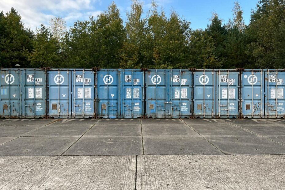 Blue shipping containers lined up outdoors against a forest background.